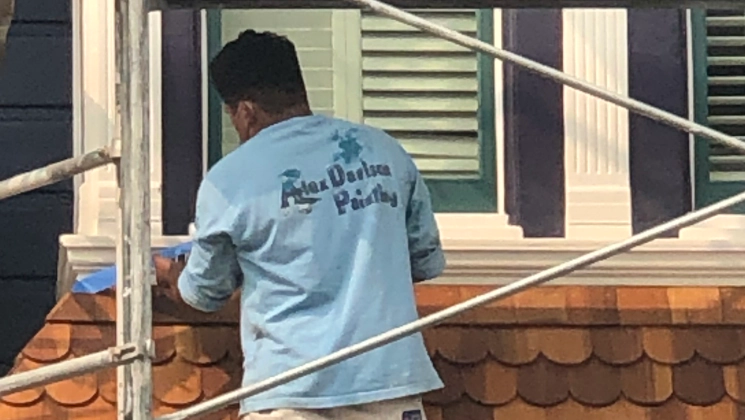 worker painting the exterior of a house with light brown tiled roofing
